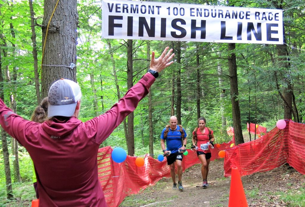 Amy greeting in two runners at the finish line of the Vermont 100, a tradition of hers