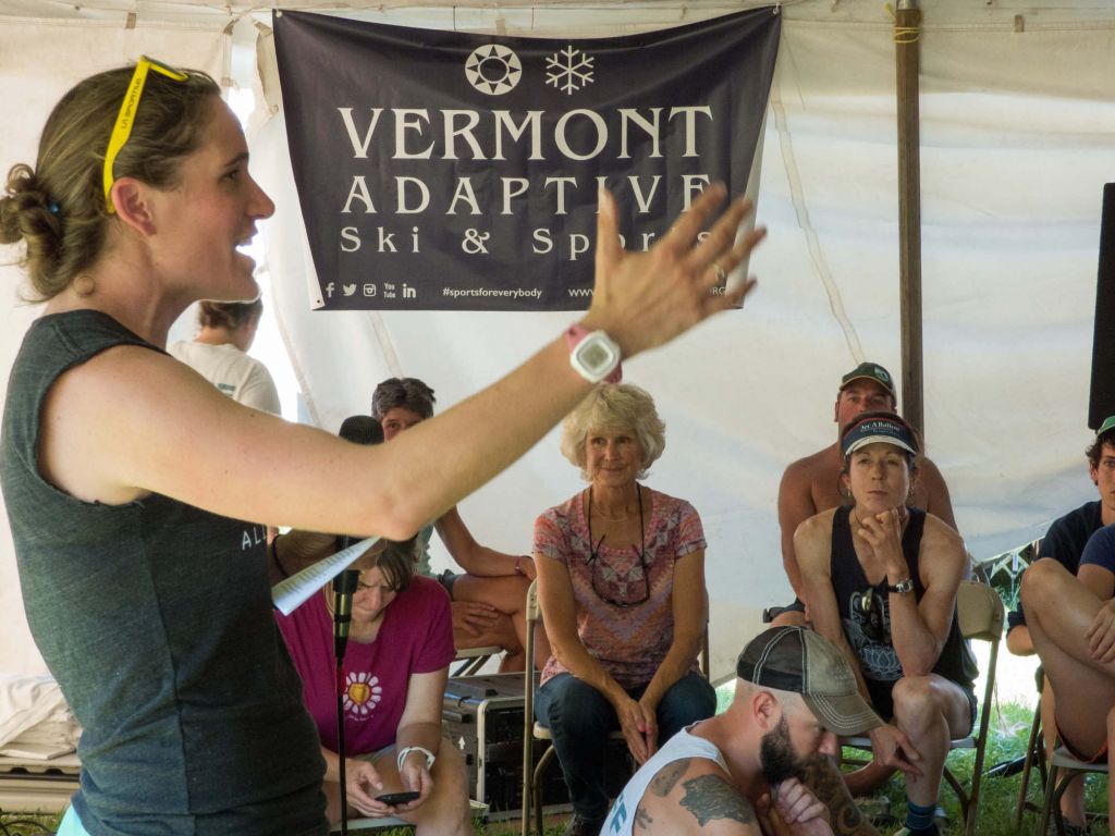 Amy speaking to the crowd at the Vermont 100 Pre-Race Meeting with a Vermont Adaptive banner hanging behind her. 