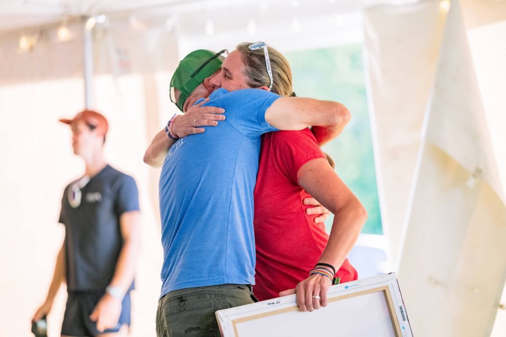 Terry Shearer at the 2026 VT100 Pre-Race Meeting Hugging RD Amy Rusiecki as He Recieves the 2026 Stoney Award for Volunteering